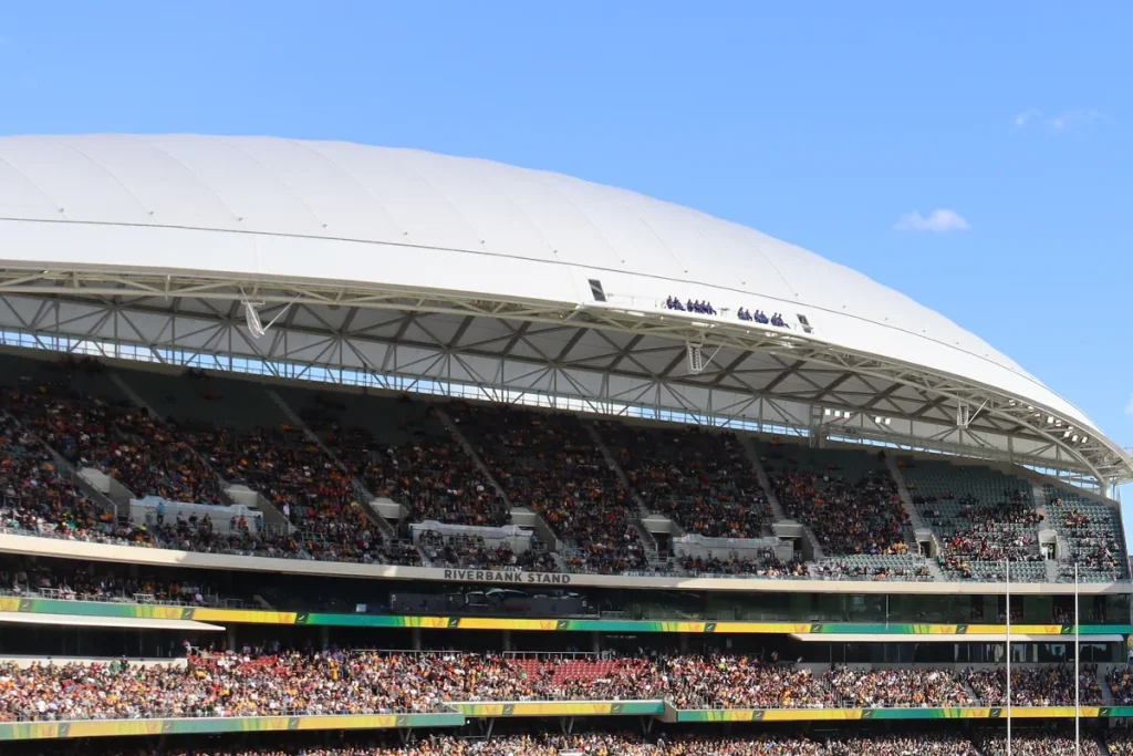 The white canopy roof and packed tiers of the Riverbank Stand at Adelaide Oval under a clear blue sky, the crowd dotted with gold Wallabies jerseys.