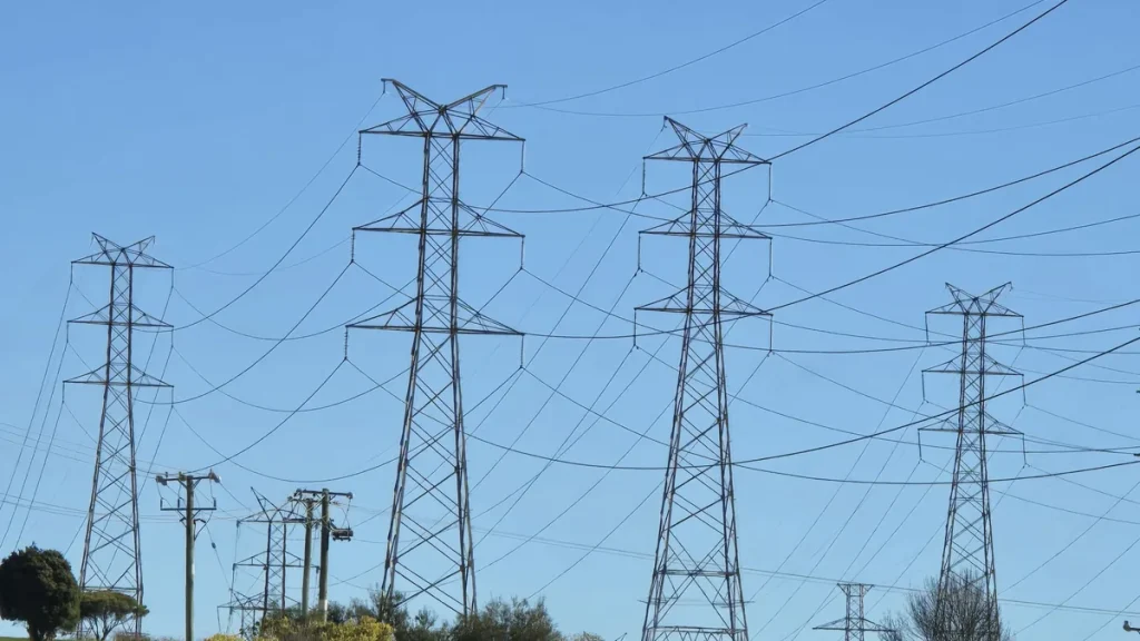 Steel lattice transmission towers carrying power lines over a green hillside at Bell Bay in northern Tasmania, photographed in August 2026.