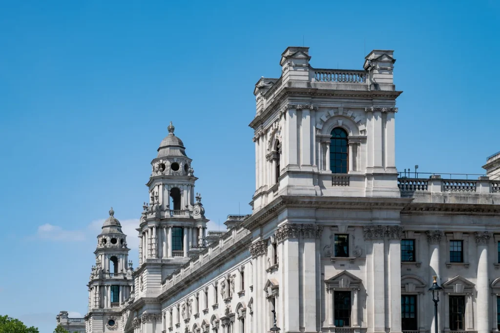 The ornate stone towers and upper floors of the HM Treasury building on Whitehall against a clear blue sky.