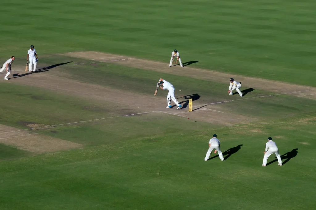 A Test match at Newlands seen from high in the stands: a bowler running in, a batter in whites at the crease and Australian fielders spread across the green outfield.