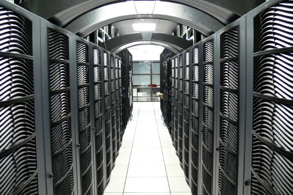 A long white-tiled aisle between two rows of tall black server cabinets with curved grille doors, lit from above.
